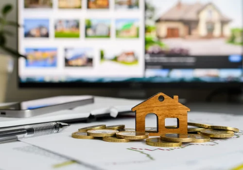 a small model of a house on top of a table with a computer screen full of house images on it